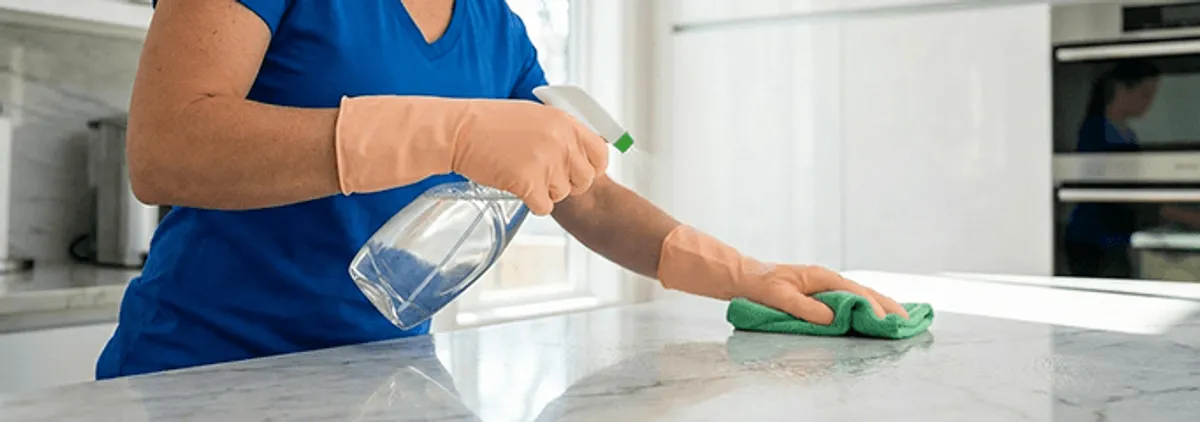 Maid service worker spraying and wiping a kitchen countertop with a microfiber cloth for sanitizing, Tallahassee, FL.